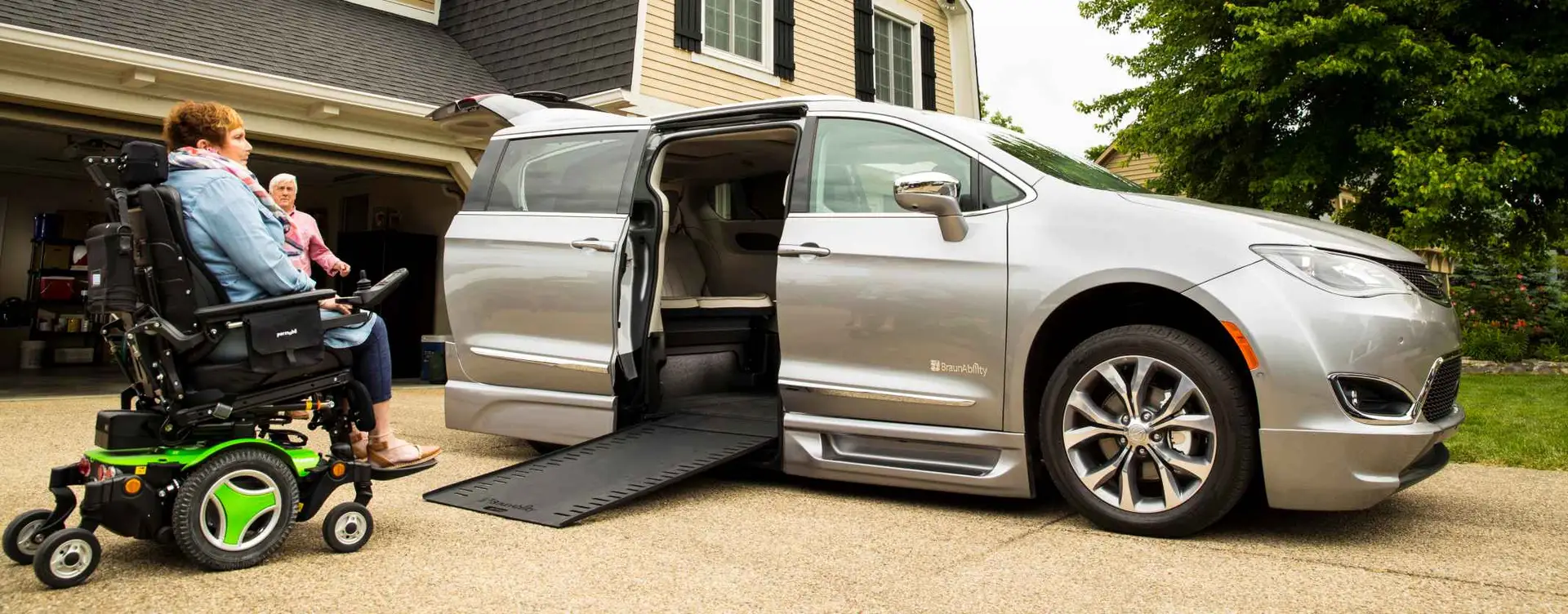 Lady in power wheelchair at her house heading up side wheelchair ramp of her gold chrysler pacifica wheelchair van from BraunAbility